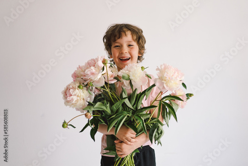 Cheerful happy child with Peonys bouquet. Smiling little boy on white background. Mother's Day. Love and romantic concept