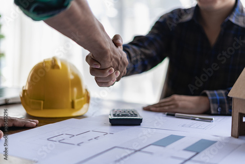 Yellow hard hat on table and house design print design with construction team handshake greeting start new project contract plan in office center at construction site partner and contractor