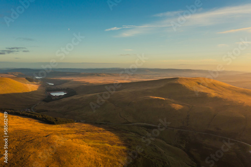 Expansive golden landscapes of Wales at sunset showcasing rolling hills and shimmering lakes in the distance