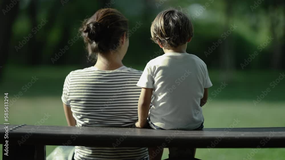 Back of mother and child sitting at park bench together. Parent and son enjoying nature in sunny day Back of mother and child sitting at park bench together. Parent and son enjoying nature in sunny day