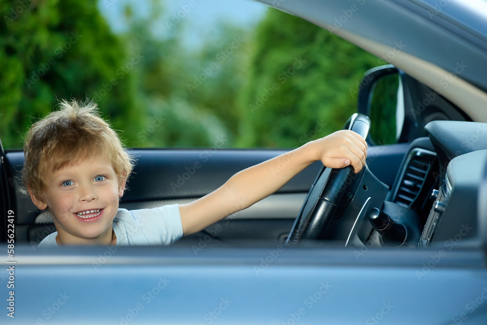 Cute little boy behind the wheel of an expensive car holds the steering wheel, happily looks into the camera. Fulfilling a child's dream of sitting behind the wheel in a real car Cute little boy behind the wheel of an expensive car holds the steering wheel, happily looks into the camera. Fulfilling a child's dream of sitting behind the wheel in a real car