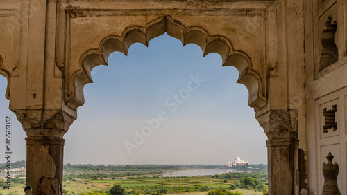 Through the openwork arched vault of the Musamman Burj Palace in the Red Fort, you can see the green valley, the lake and the beautiful Taj Mahal in the distance. India. Agra
