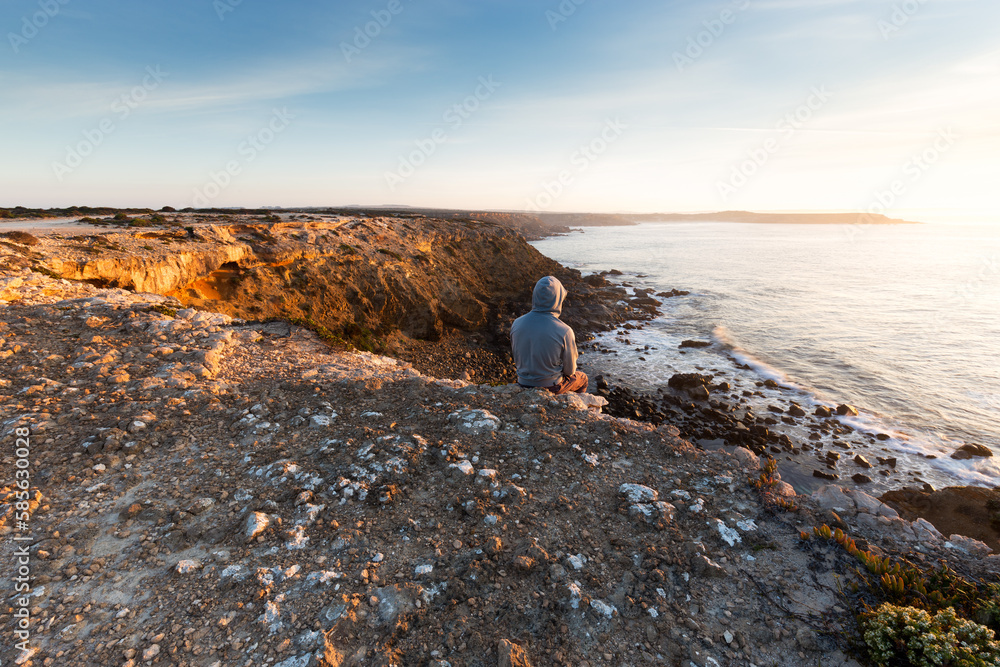 Person sitting on a cliff looking at rugged coast view and surf during golden sunrise in South Australia