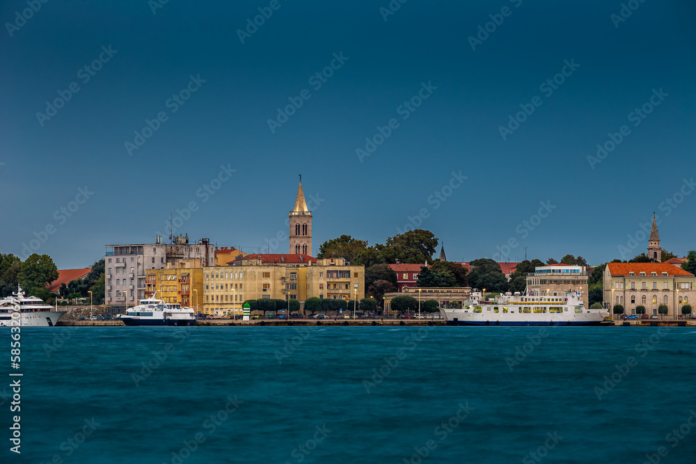 Zadar, Croatia - Panoramic view of the old town of Zadar at sunset with illuminated Cathedral of St. Anastasia bell tower, yachts and ferry and clear blue sky on a summer afternoon