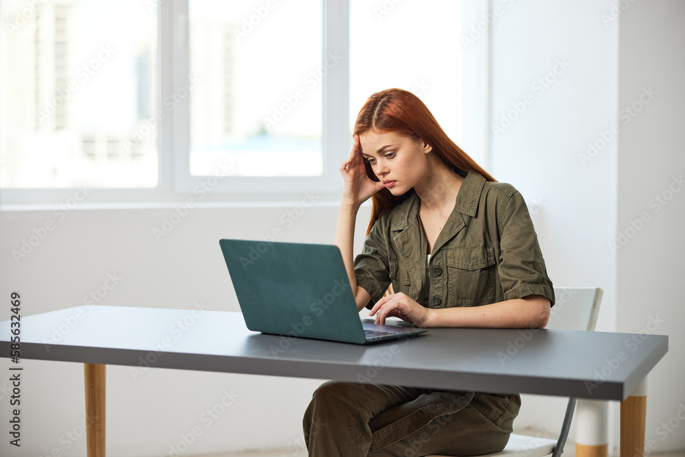 portrait of a red-haired woman in the office sitting thoughtfully at a laptop portrait of a red-haired woman in the office sitting thoughtfully at a laptop