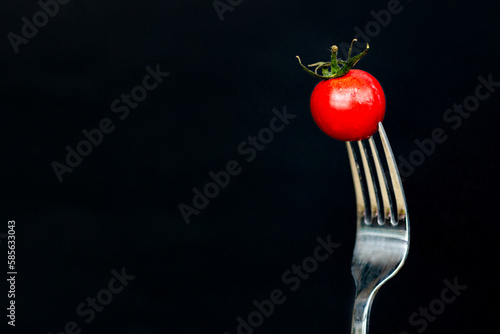 Minimal macro photography of fresh tomato on fork on black background with copy space. Mockup template for keto diet or receipt book