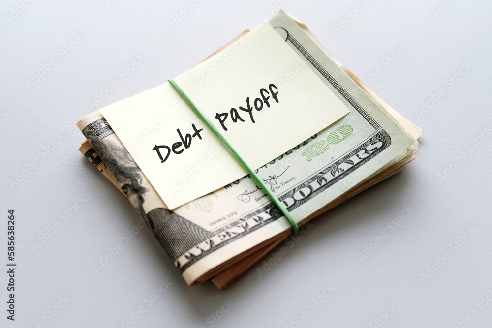 Dollars cash money in rubber band with text written note DEBT PAYOFF , on copy space background - concept of financial planning to save money for purpose of getting out of debt Dollars cash money in rubber band with text written note DEBT PAYOFF , on copy space background - concept of financial planning to save money for purpose of getting out of debt