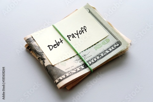 Dollars cash money in rubber band with text written note DEBT PAYOFF , on copy space background - concept of financial planning to save money for purpose of getting out of debt