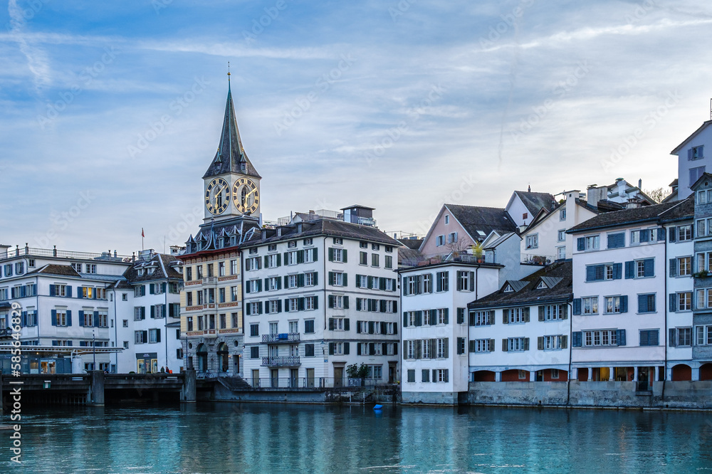 Old City of Zurich (Niederdörfli, Zürich) shot from the riverside (Limmat). The church Fraumünster with his shiny dial is behind old and beautiful buildings.