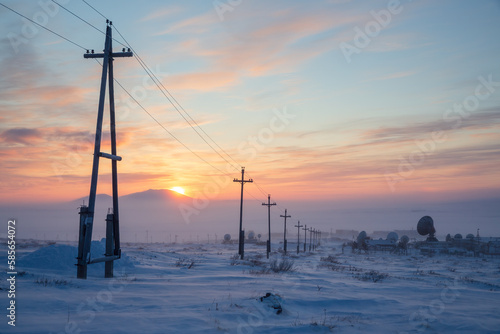Electric poles and large satellite dishes in the snowy winter tundra. Winter arctic landscape. Cold frosty winter weather. The sun is setting behind the mountain. Chukotka, Siberia, Far East of Russia © Andrei Stepanov