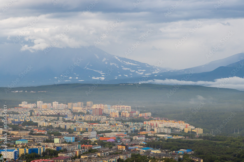 Summer cityscape. Top view of the buildings and streets of the city. Residential urban areas. Volcanoes in the distance. Cloudy rainy weather. Petropavlovsk-Kamchatsky, Kamchatka, Far East of Russia.