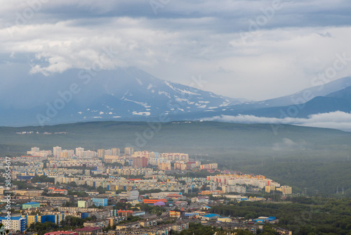 Summer cityscape. Top view of the buildings and streets of the city. Residential urban areas. Volcanoes in the distance. Cloudy rainy weather. Petropavlovsk-Kamchatsky, Kamchatka, Far East of Russia.
