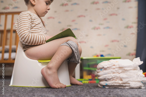 Potty training concept. A three-year-old boy sits on a potty in a children's room among toys and  read a book.  photo