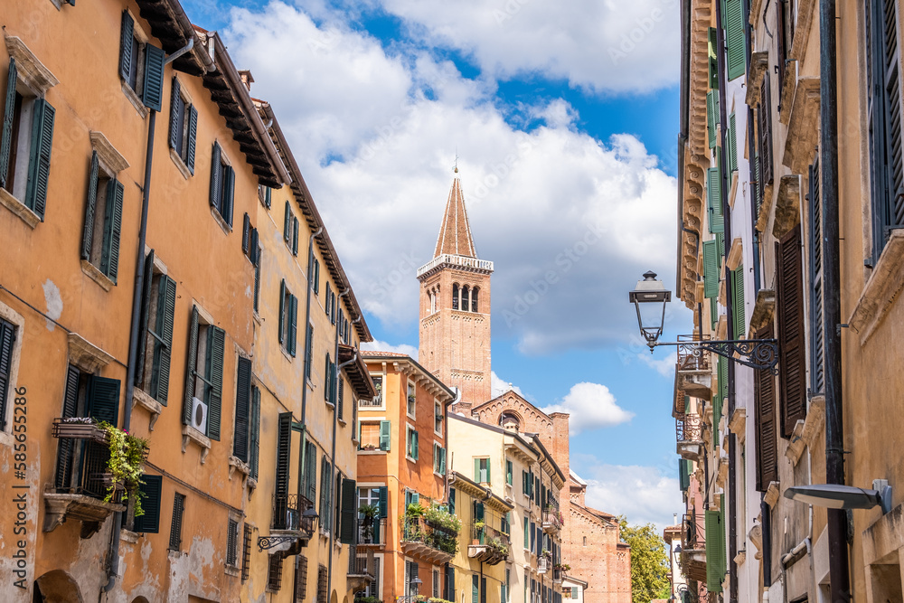 An alley in Verona with terraces with green plants and the bell tower of a church