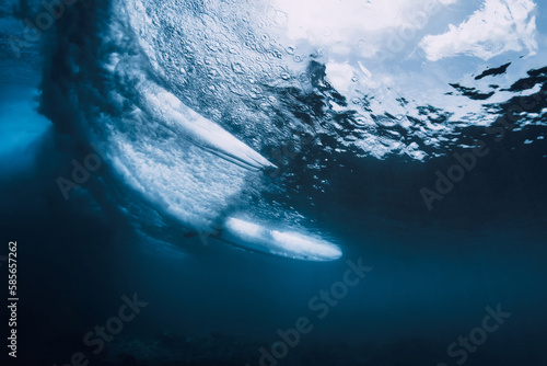 Wave underwater and surfer riding on surfboard in ocean. Underwater crashing wave and surfboard in transparent water