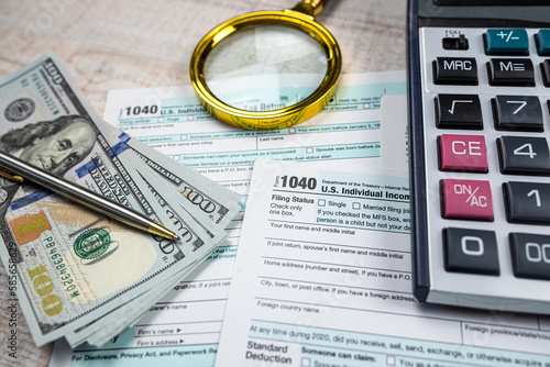 magnifying glass and us dollars bills and calculator on 1040 individual income tax return form