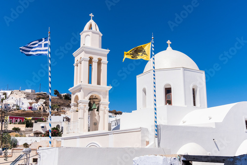 Church and bell tower in typical Greek style in Santorini with flag of Greece and yellow Double-headed eagle