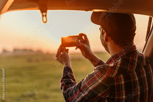 Handsome man using mobile phone in the car during a road trip on sunset.