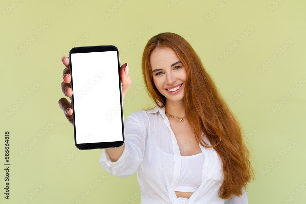 Beautiful red hair woman in casual shirt on green background holds a phone with a blank white screen Beautiful red hair woman in casual shirt on green background holds a phone with a blank white screen