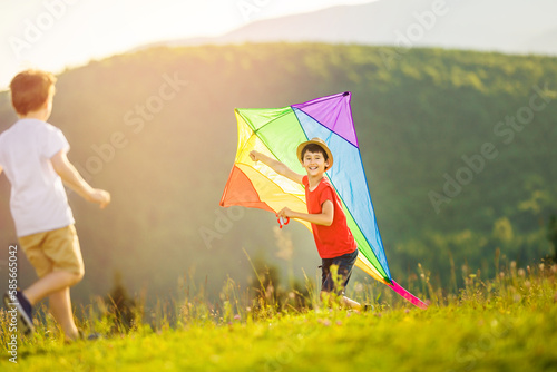 Little boys family play with large kite in summertime on meadow in tall grass. Children's active sports and outdoor activities. Happy childhood moments.
