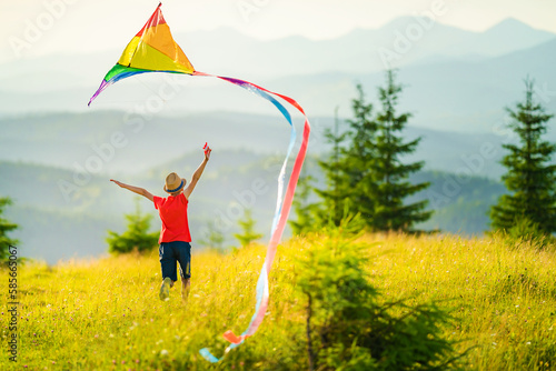 Little school age boy running down the slope with kite in the sun. Sunny summer or spring day at sunset. Active outdoor games and leisure.