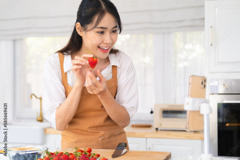 Female chef holding strawberry , shooting video using camera on tripod. baker online courses,live stream . Food blogger healthy food in kitchen.Social media influencer. Food blogger creating content. Female chef holding strawberry , shooting video using camera on tripod. baker online courses,live stream . Food blogger healthy food in kitchen.Social media influencer. Food blogger creating content.