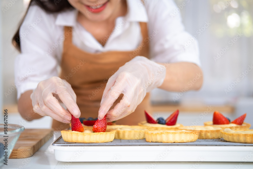 Closeup of hands in cooking gloves decorating freshly baked tart with blueberries strawberry fresh fruit.housewife baker wear apron making fruit tart. homemade bakery at home. Closeup of hands in cooking gloves decorating freshly baked tart with blueberries strawberry fresh fruit.housewife baker wear apron making fruit tart. homemade bakery at home.