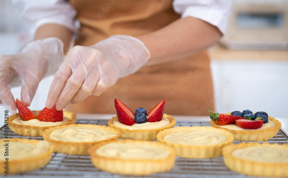Closeup of hands in cooking gloves decorating freshly baked tart with blueberries strawberry fresh fruit.housewife baker wear apron making fruit tart. homemade bakery at home. Closeup of hands in cooking gloves decorating freshly baked tart with blueberries strawberry fresh fruit.housewife baker wear apron making fruit tart. homemade bakery at home.