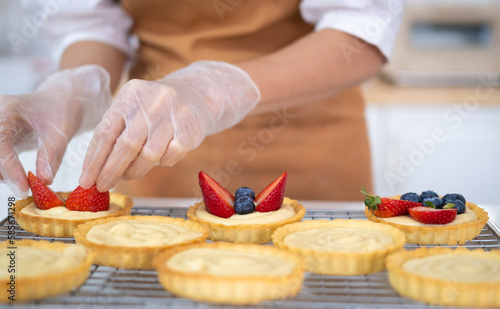 Closeup of hands in cooking gloves decorating freshly baked tart with blueberries strawberry fresh fruit.housewife baker wear apron making fruit tart. homemade bakery at home.
