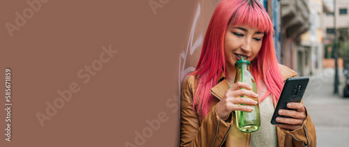 smiling young woman having a soft drink while chatting with the phone in the street