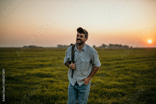 A handsome man in casual wear walks on a grassy field, having a backpack, and enjoys the fresh air. Digital nomad concept