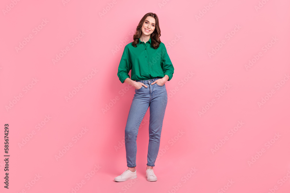 Full length photo of satisfied lovely nice person wear jeans green shirt sneakers standing arms in pockets isolated on pink background Full length photo of satisfied lovely nice person wear jeans green shirt sneakers standing arms in pockets isolated on pink background