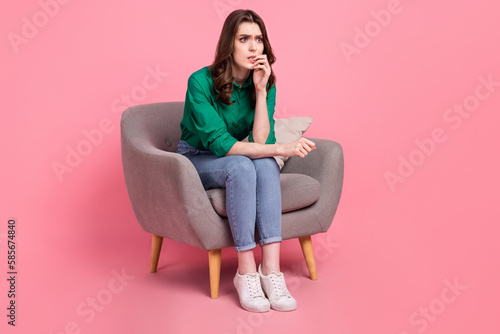 Full length photo of worried nervous woman wear green shirt look empty space sit on armchair look for solution isolated on pink background