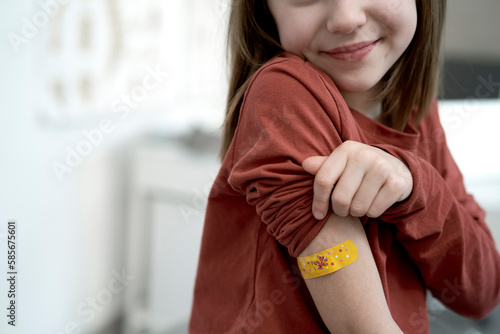 Smiling girl showing adhesive bandage after vaccination in clinic