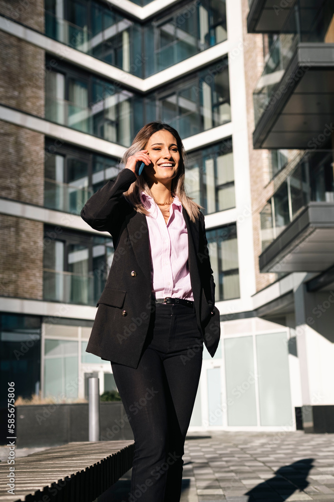 Smiling businesswoman talking on smart phone outside office building Smiling businesswoman talking on smart phone outside office building