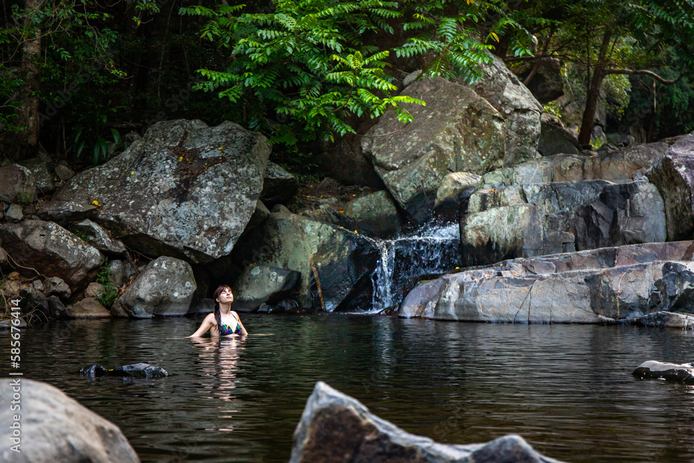 a beautiful girl in a bikini takes a refreshing swim at a waterfall at