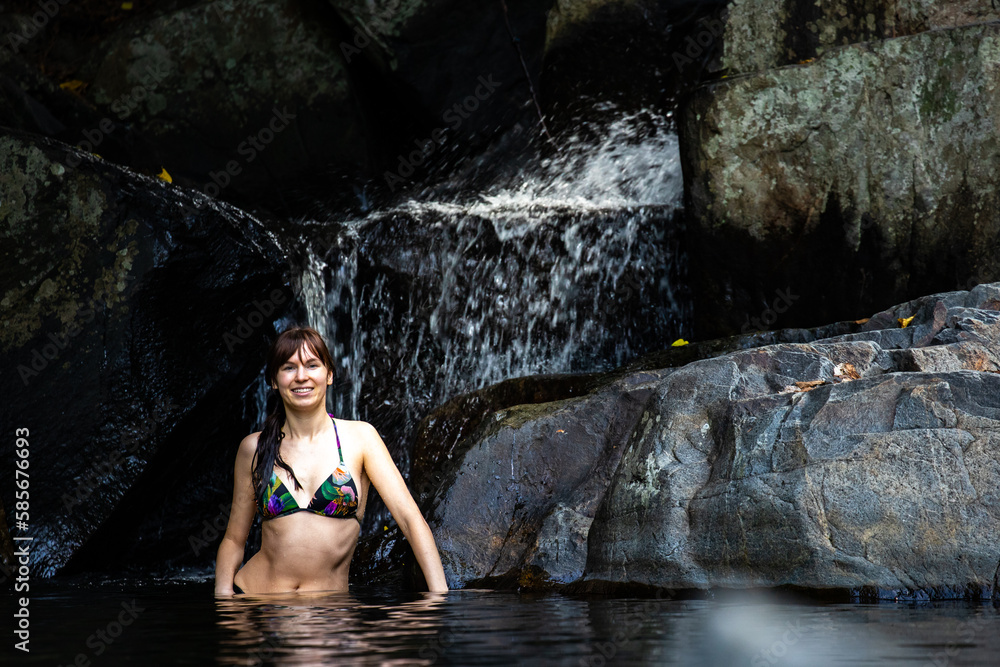 a beautiful girl in a bikini takes a refreshing swim at a waterfall at