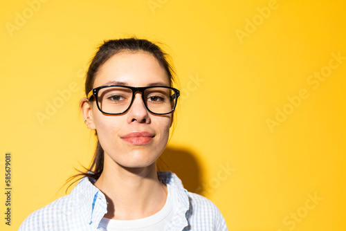 Smiling young woman wearing eyeglasses against yellow background photo