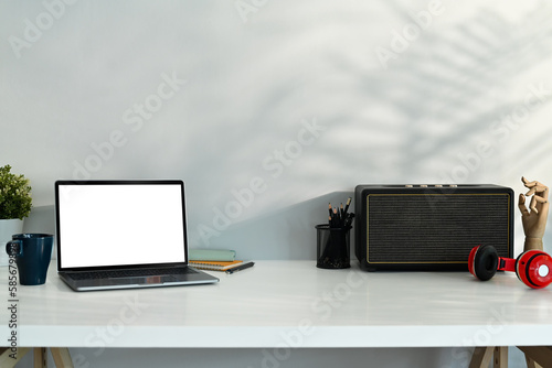 Stylish workplace with laptop computer, wireless speaker and headphone on white table