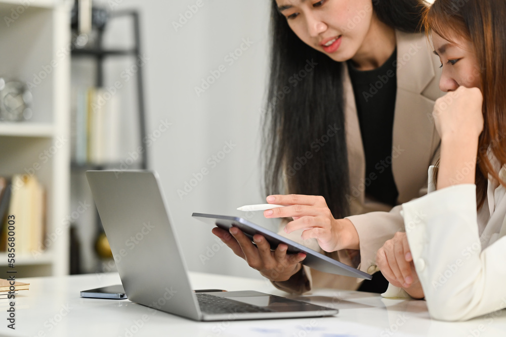 Two businesswomen using a digital tablet, collaborating on a new project at co working space in office Two businesswomen using a digital tablet, collaborating on a new project at co working space in office