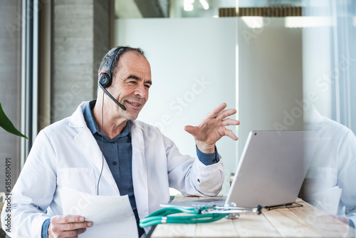 Wallpaper Mural Smiling mature doctor explaining over telemedicine video call at desk Torontodigital.ca