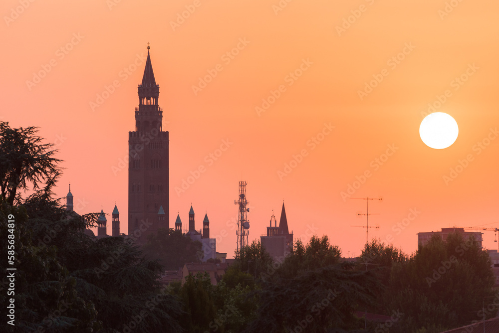 Sunset over Cremona with the imposing silhouette of the Torrazzo, bell tower of the Cathedral in beautiful market square Piazza Duomo. Lombardy, Italy.