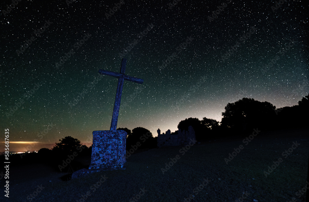 Obraz premium Long Exposure night photograph with stars in the background and foreground a cross and trees