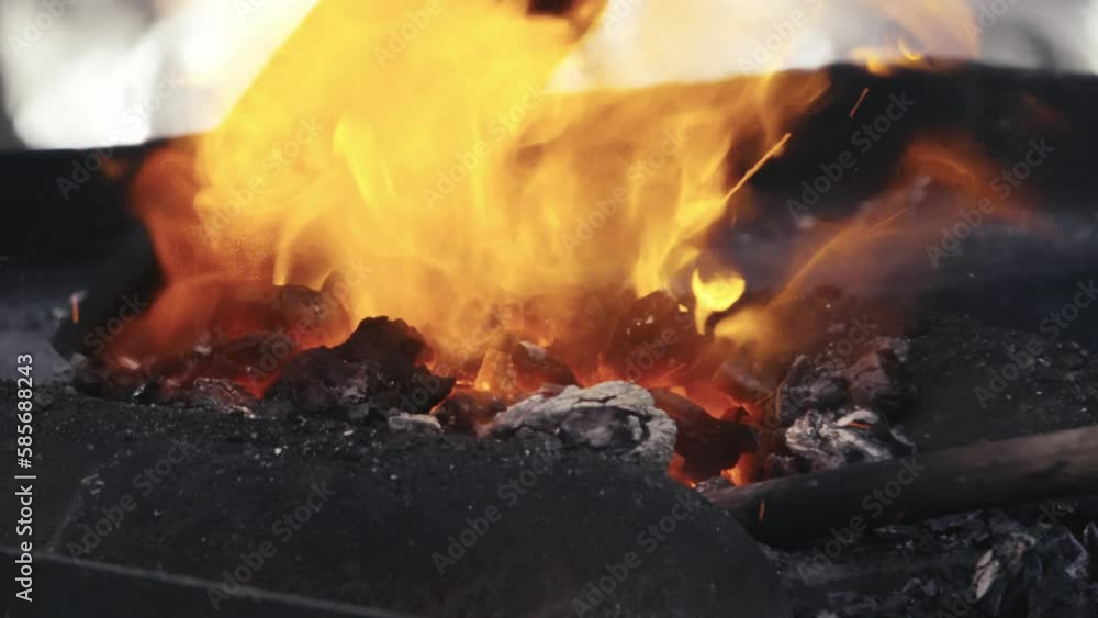 A blacksmith scoops hot coals onto a molten metal rod. Slow motion close up shot. A blacksmith scoops hot coals onto a molten metal rod. Slow motion close up shot.
