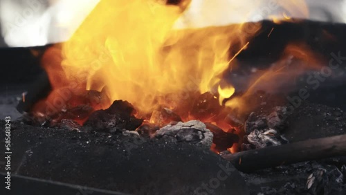 A blacksmith scoops hot coals onto a molten metal rod. Slow motion close up shot.