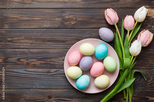 Happy Easter composition. Easter eggs in basket on colored table with yellow Tulips. Natural dyed colorful eggs background top view with copy space