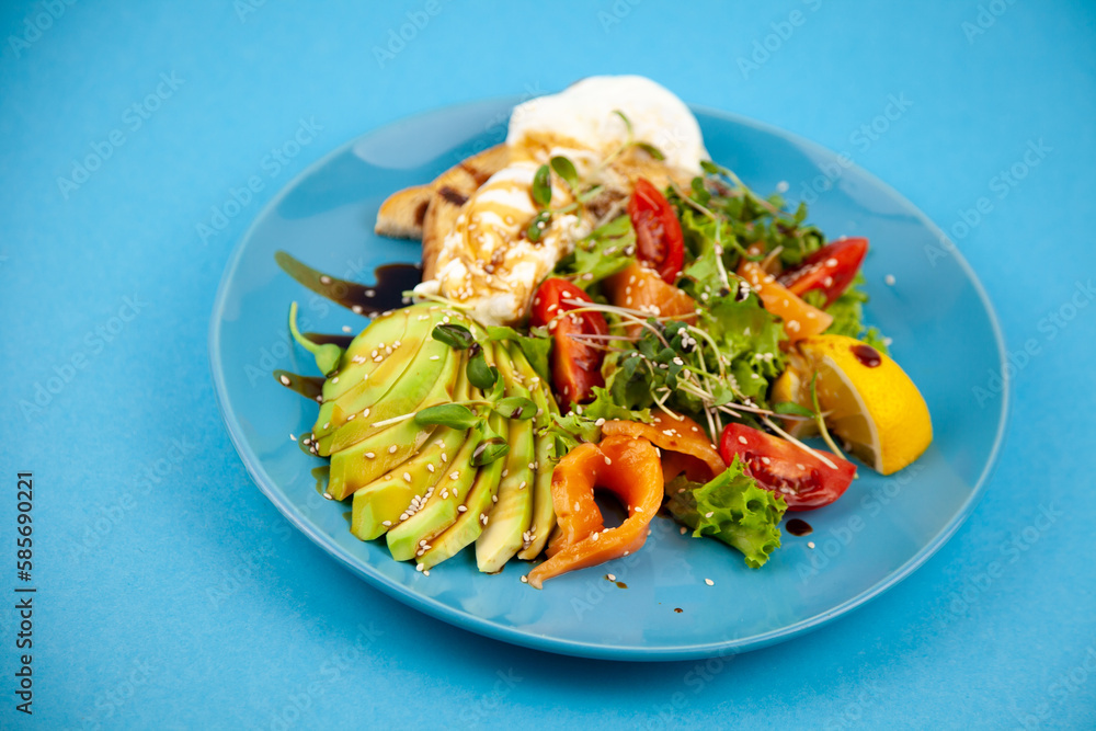 Healthy breakfast. Avocado and salmon, poached egg and toast, salad and vegetables. Microgreens on a plate. Food bowl. Lunch on a blue plate. Sauce and sesame seeds, lemon tomatoes. Top view. Healthy breakfast. Avocado and salmon, poached egg and toast, salad and vegetables. Microgreens on a plate. Food bowl. Lunch on a blue plate. Sauce and sesame seeds, lemon tomatoes. Top view.