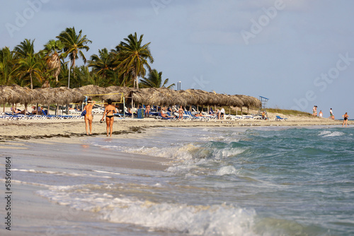 Tropical beach with tanning people and coconut palm trees. Ocean coast, tourist resort on Caribbean islands