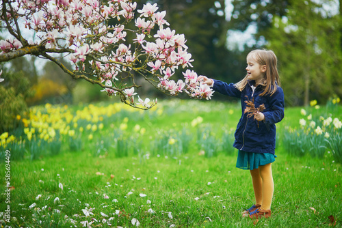 Adorable preschooler girl enjoying nice spring day in park during magnolia blooming season