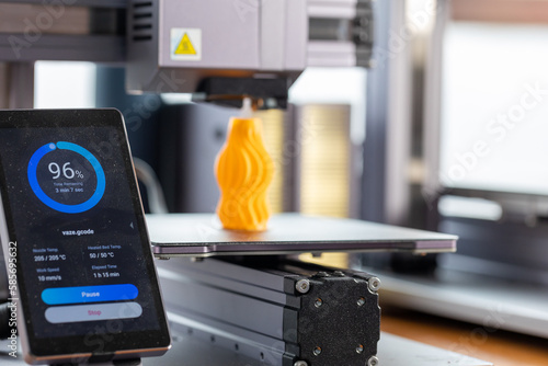 Application for control 3D printer displayed on smartphone. Against the background, a 3D printer prints detail